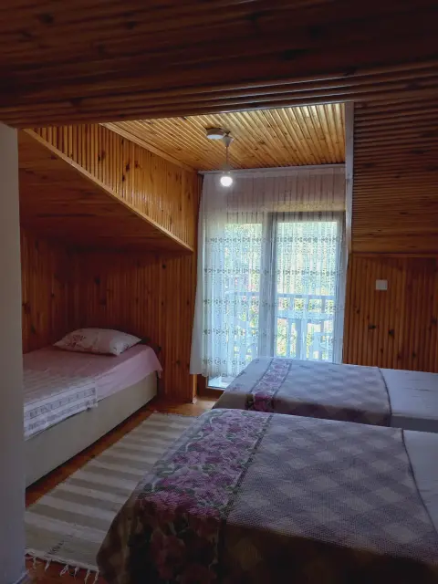 3 Kişilik Oda: Ahşap tavanlı odada yataklar ve pencere
